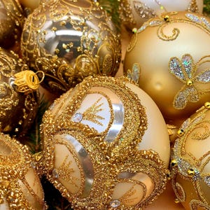 以下が含まれることがあります： 複雑なデザインの金色のクリスマスオーナメントのクローズアップ。 いくつかのオーナメントには、グリッターとビーズの装飾が施されています。 オーナメントはさまざまなゴールドとクリームの色合いで、お祝いのホリデーディスプレイを作成します。