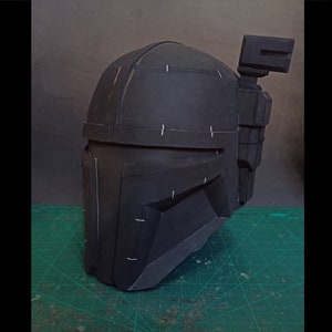 May include: A black helmet with a textured surface and a small rectangular attachment on the side. The helmet has white lines drawn on it.