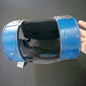 May include: A blue and gray plastic chest piece with straps. The chest piece has two blue panels with rectangular cutouts.