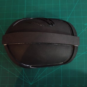 May include: A black foam knee pad with a black elastic strap. The pad has a white line around the edge.