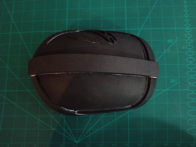 May include: A black foam knee pad with a black elastic strap. The pad has a white line around the edge.
