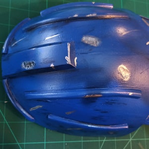 May include: A blue hard hat with silver paint accents and scratches. The hard hat is made of plastic and has a rounded shape.
