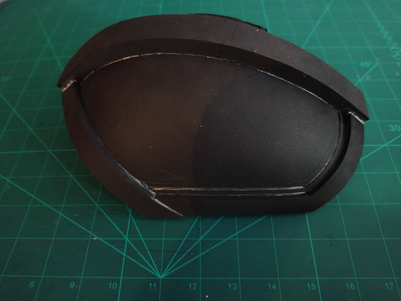 May include: A black foam piece with a curved shape and a raised edge. The foam piece has been painted black and has a smooth surface.