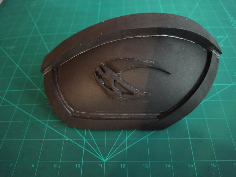 May include: A black foam mold with a raised, stylized crescent moon design. The mold is on a green cutting mat.