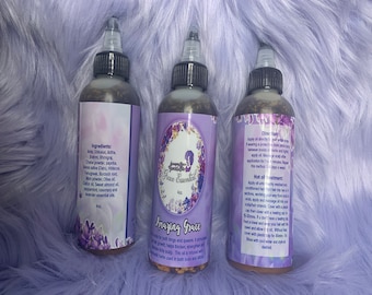 May include: Three brown glass bottles with labels that say "Amazing Grace" and "Face Essentials". The bottles contain a dark liquid and have ingredients listed on the back. The bottles are on a purple fuzzy surface.