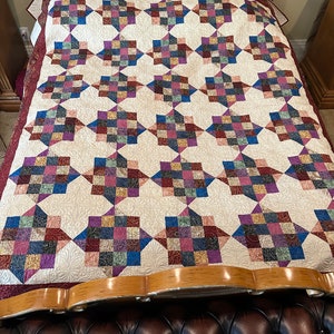 May include: A quilt with a patchwork design featuring a variety of colors, including red, blue, green, and purple. The quilt is made up of squares and diamonds, and it has a white background. The quilt is on a bed with a wooden headboard.