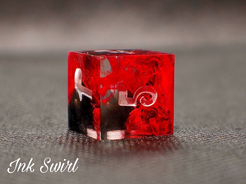 May include: A red and black dice with white ink swirl and numbers. The dice is made of clear resin and has a swirling pattern.