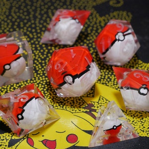 May include: Set of six clear dice with red and white Pokeball designs. The dice are made of clear resin and have a frosted finish. The Pokeball designs are painted on the dice and are visible through the clear resin.