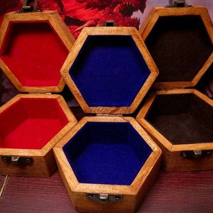 Op de afbeelding: Vijf zeshoekige houten dozen met scharnierende deksels. Elke doos is bekleed met een ander gekleurd vilt: rood, blauw en zwart. De dozen zijn in een halve cirkel gerangschikt.