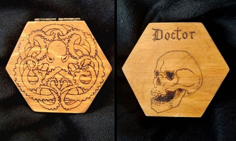 May include: Hexagonal wooden box with a hinged lid. One side features an etched octopus design surrounded by gears. The other side has the word "Doctor" above a skull illustration. The box is made of light-coloured wood.