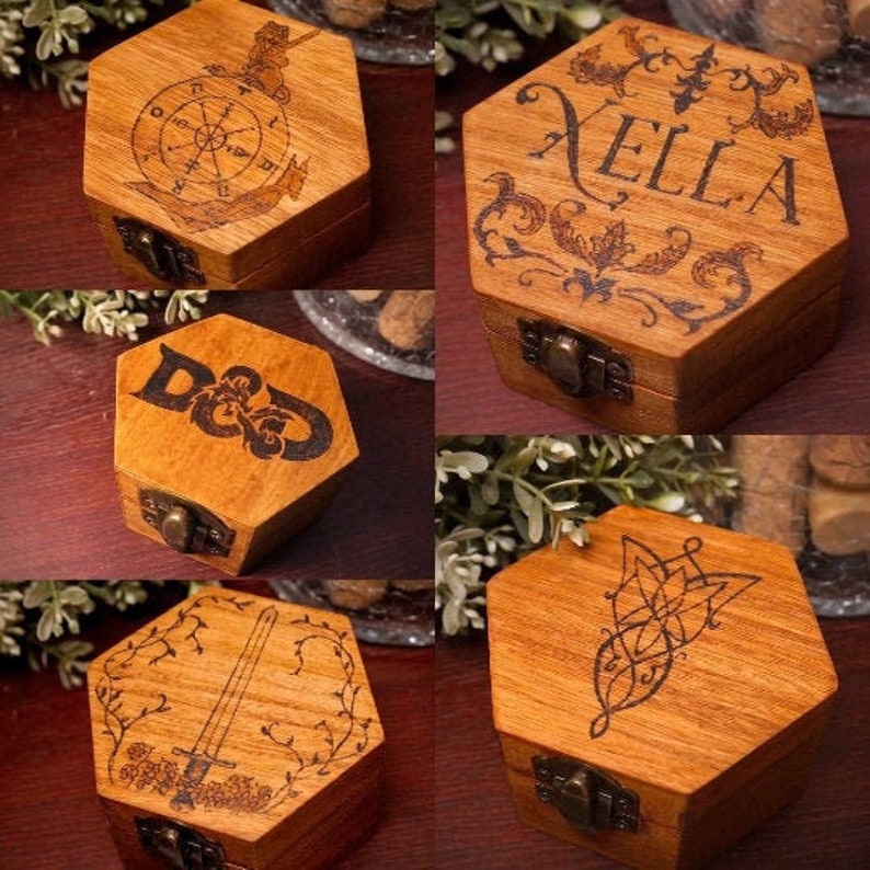 May include: Hexagonal wooden boxes with hinged lids. Each box features a dark-etched design: a compass, the name "Xella", the letters "D&D", a sword, and a floral emblem. The boxes have metal clasps.