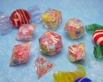 May include: A set of pink and white dice with candy cane and swirl designs. The dice are made of clear plastic and filled with colorful candy-like pieces. The dice are on a light blue surface.