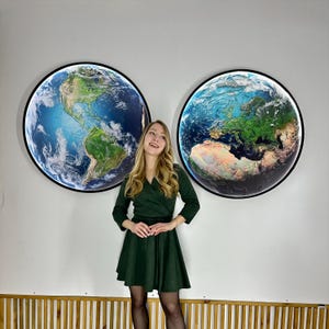 May include: Two large, round wall art pieces depicting Earth, with continents and oceans in vibrant colors. Each piece is framed in black. The image also shows a person wearing a dark green dress.