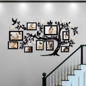 May include: A black wall-mounted family tree photo frame with multiple picture frames. The tree design includes branches, leaves, birds, and flower accents. The frames hold family photos, creating a decorative and personalized wall display.