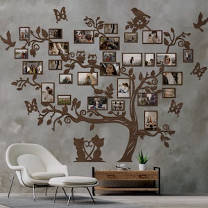 Puede incluir: Una decoraci&oacute;n de pared de &aacute;rbol geneal&oacute;gico de madera marr&oacute;n con m&uacute;ltiples marcos de fotos, que muestran im&aacute;genes de personas y animales. El &aacute;rbol est&aacute; decorado con p&aacute;jaros, mariposas y b&uacute;hos. El &aacute;rbol est&aacute; montado en una pared gris con una silla blanca y una mesa de madera delante.
