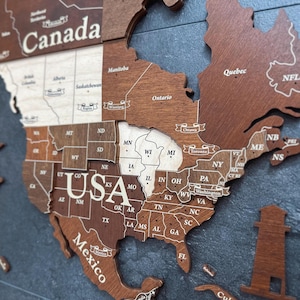 May include: Wooden map of North America, with the USA, Canada, and Mexico highlighted. The map is made of various shades of brown wood, with state and country names engraved in white. The map includes the states of the USA, and provinces of Canada.