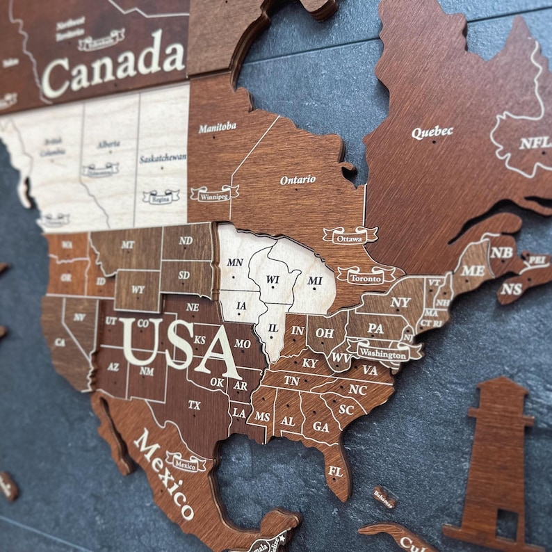 May include: Wooden map of North America, with the USA, Canada, and Mexico highlighted. The map is made of various shades of brown wood, with state and country names engraved in white. The map includes the states of the USA, and provinces of Canada.