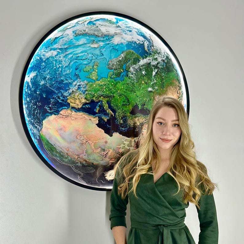 May include: A large, round wall art piece depicting a detailed, illuminated map of Earth. The artwork features vibrant blues, greens, and browns, with a black frame. The continents and oceans are clearly defined, creating a striking visual display.