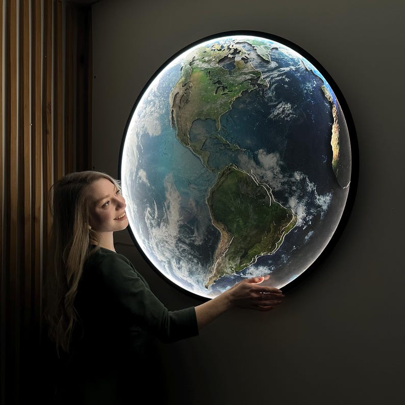 May include: A round, illuminated wall art piece depicting Earth. The artwork features a detailed map of the continents and oceans, with a bright, glowing edge. The piece is set against a dark background, creating a striking visual effect.