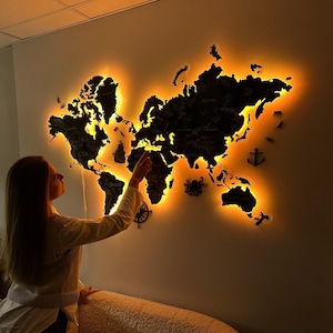 May include: A black wooden world map with a warm orange backlight, mounted on a wall. The map features etched country outlines and city names. Decorative nautical elements, such as an anchor and compass, are placed around the map.