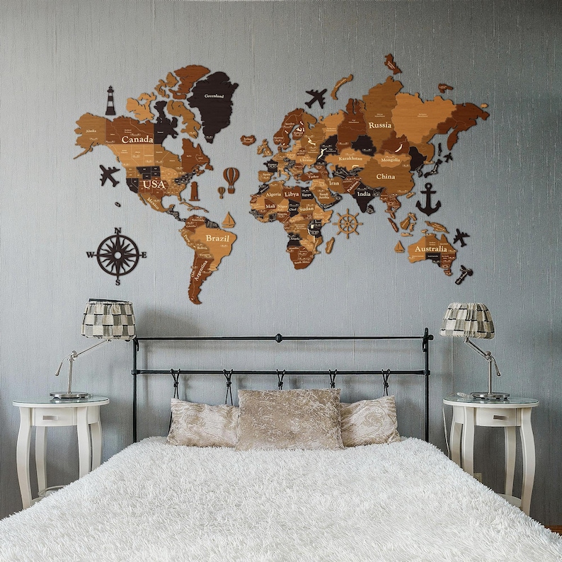 May include: A wooden world map wall decor in shades of brown and tan, mounted on a light gray wall. The map includes country names and decorative elements like airplanes and a compass. The map is above a bed with a fluffy white comforter.