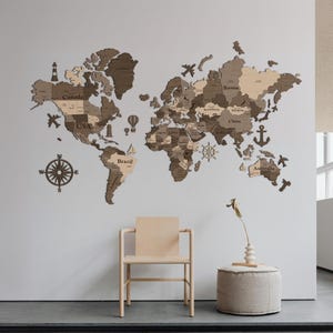 May include: A wooden world map wall decor in shades of brown and tan, with country outlines and decorative icons like airplanes and a compass. The map is mounted on a white wall, with a chair and ottoman in front.