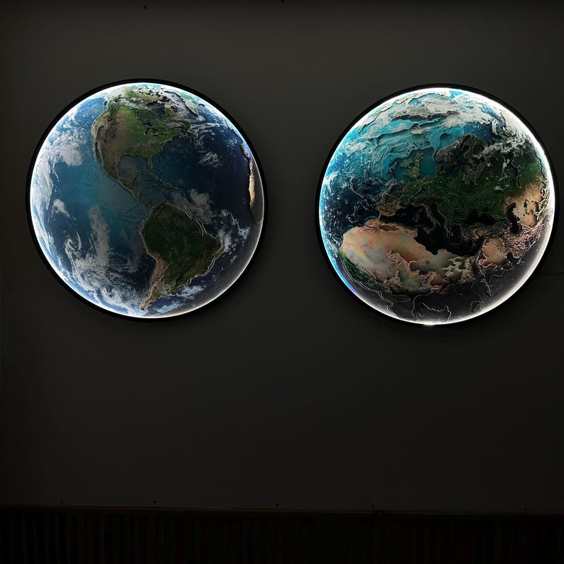 May include: Two illuminated, round wall art pieces depicting Earth. One shows the Americas, the other shows Europe, Africa, and Asia. The globes have a black border and a bright white light around the edge, creating a striking contrast against the dark background.