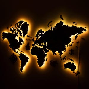 May include: A black world map with a warm yellow outline, creating a glowing effect. Decorative nautical elements, including an anchor and compass, are visible. This illuminated map is a striking piece of home decor.