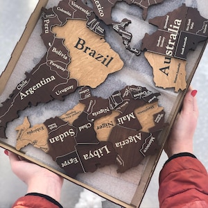 May include: A wooden world map puzzle with country outlines and names. The map is in a wooden tray, with countries like Brazil, Argentina, and Australia visible. The map is made of light and dark brown wood.