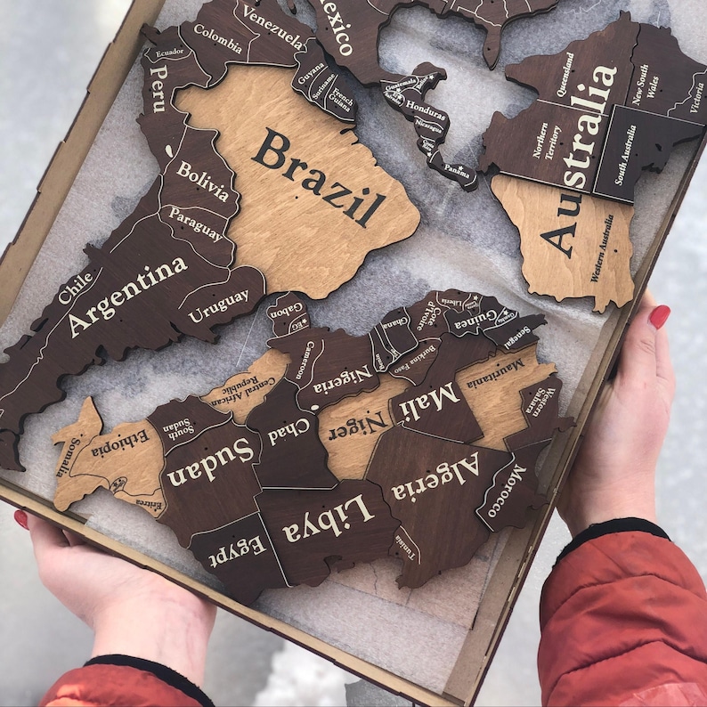 May include: A wooden world map puzzle with country outlines and names. The map is in a wooden tray, with countries like Brazil, Argentina, and Australia visible. The map is made of light and dark brown wood.