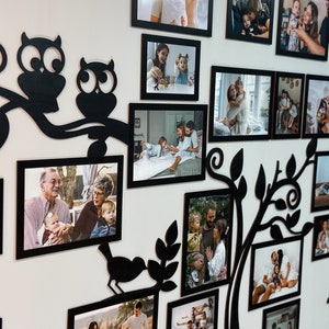 Puede incluir: Una silueta negra de un &aacute;rbol con ramas y hojas, con m&uacute;ltiples marcos de fotos negros colgados en una pared blanca. Los marcos contienen fotos de una familia, incluidos ni&ntilde;os, adultos y abuelos. La silueta del &aacute;rbol tiene dos b&uacute;hos y un p&aacute;jaro en las ramas.