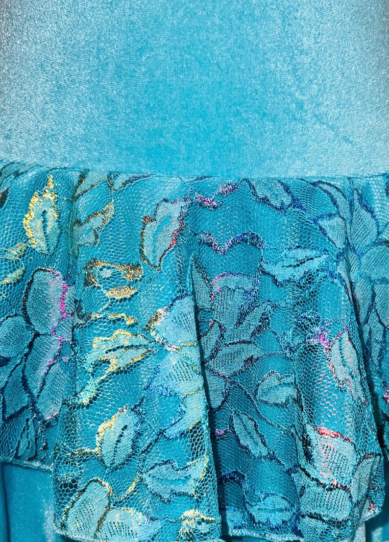 Pu&ograve; includere: Un tessuto blu turchese con uno strato di pizzo blu turchese con accenti dorati e argentati.