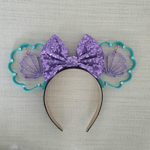 May include: Purple and teal Minnie Mouse ears with a purple sequined bow and a seashell design.