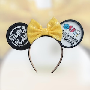 May include: A black headband with a yellow sequined bow and two circular ear accents. One ear has the text "SIMPLE PLAN" in white, and the other has the text "This is where I belong" with a sad face, broken heart, and rain cloud graphic.