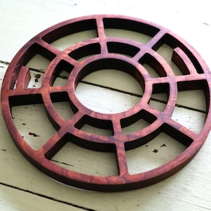 May include: A round wooden coaster with a geometric design. The coaster is made of dark wood and has a circular cutout in the center.