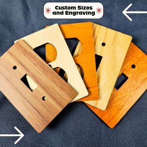 Pode incluir: Uma coleção de espelhos de parede retangulares de madeira para interruptores e tomadas em vários tons e padrões de veios de madeira. As placas possuem recortes para interruptores e tomadas. Uma etiqueta diz Custom Sizes and Engraving.