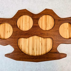 May include: A wooden serving tray with a unique design. The tray features four circular cutouts and a central, curved section, all made of light-colored bamboo. The surrounding frame is a rich, dark brown.