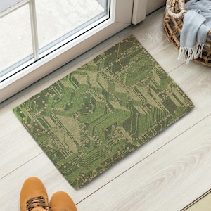 May include: A rectangular doormat with a green circuit board design. The mat is made of a woven material and has a beige and green color scheme. The doormat is placed in front of a door.