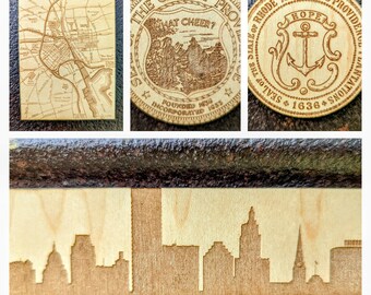 Może przedstawiać: Kolekcja drewnianych przedmiotów z wycinanymi laserowo wzorami. Zawiera mapę Providence, Rhode Island, pieczęć miejską, pieczęć stanową z kotwicą i sylwetkę panoramy miasta. Przedmioty są jasnobrązowe.