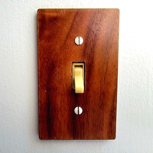 May include: A rectangular light switch cover plate with a dark brown wood grain finish. The plate features a central toggle switch in a light beige colour with the word OFF printed on it, secured by two flat-head screws with a silver finish.