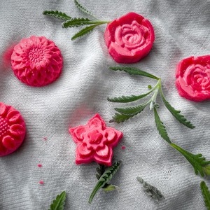 Peut inclure: Cinq savons en forme de fleurs roses sur un fond de tissu blanc. Les savons sont en forme de rose, de tournesol, d'étoile et de deux autres roses.