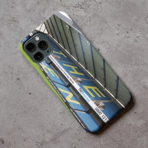 May include: A phone case featuring a photograph of a stadium seating area. The seats are blue and yellow and the text "TW Drainage 0800 121" is visible on the case.