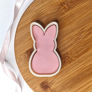 May include: A pink bunny-shaped cookie cutter on a wooden surface.
