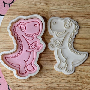 May include: Two dinosaur-shaped cookie cutters, one pink and one white. The cutters are made of plastic and have a detailed design.
