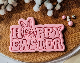 May include: Pink silicone mold for baking cookies or fondant. The mold features a bunny rabbit with the words "Hoppy Easter" in a retro font.