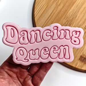 May include: Pink plastic cookie cutter with the words "Dancing Queen" in a retro font.