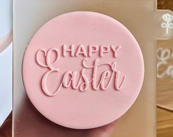 May include: A clear acrylic stamp with a pink background and the text "Happy Easter" in white. The stamp is on a wooden surface.