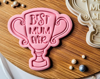 Puede incluir: Un cortador de galletas de plástico rosa y blanco con forma de trofeo con el texto "Best Mum Ever" en él.