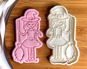 Puede incluir: Dos cortadores de galletas de plástico con forma de bruja sosteniendo una escoba. El cortador de la izquierda es rosa y el de la derecha es blanco.