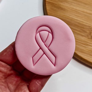 May include: Pink silicone stamp featuring a pink ribbon design. The stamp is used for baking and decorating cookies, cakes, and other treats.